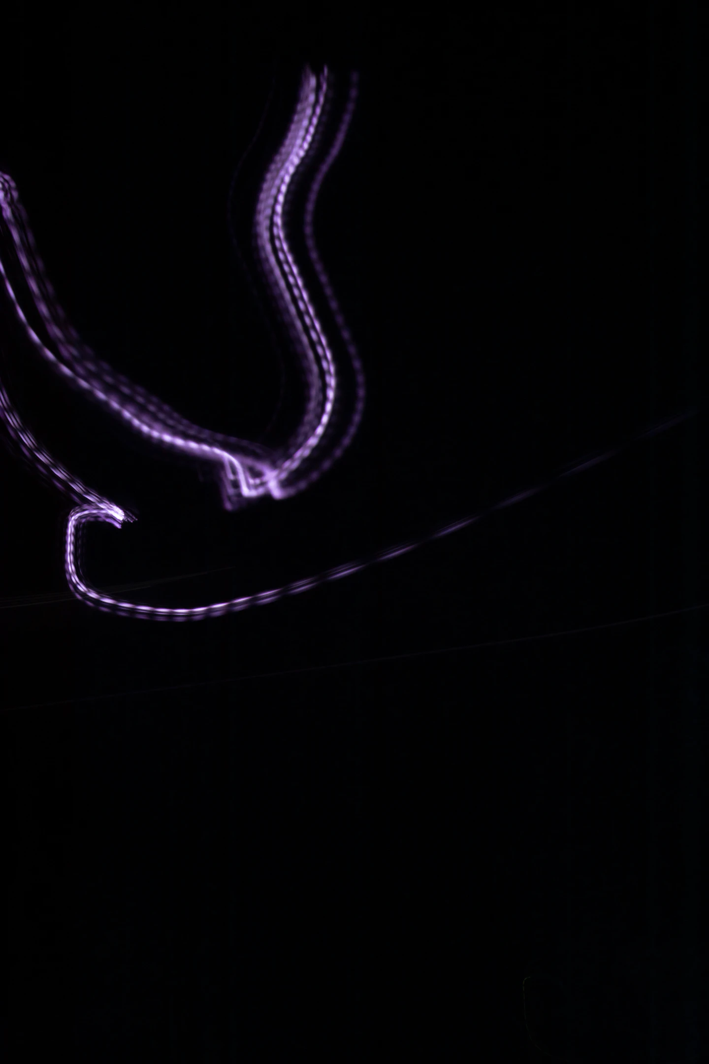 Traînées lumineuses violettes dessinant des courbes sur un fond noir.