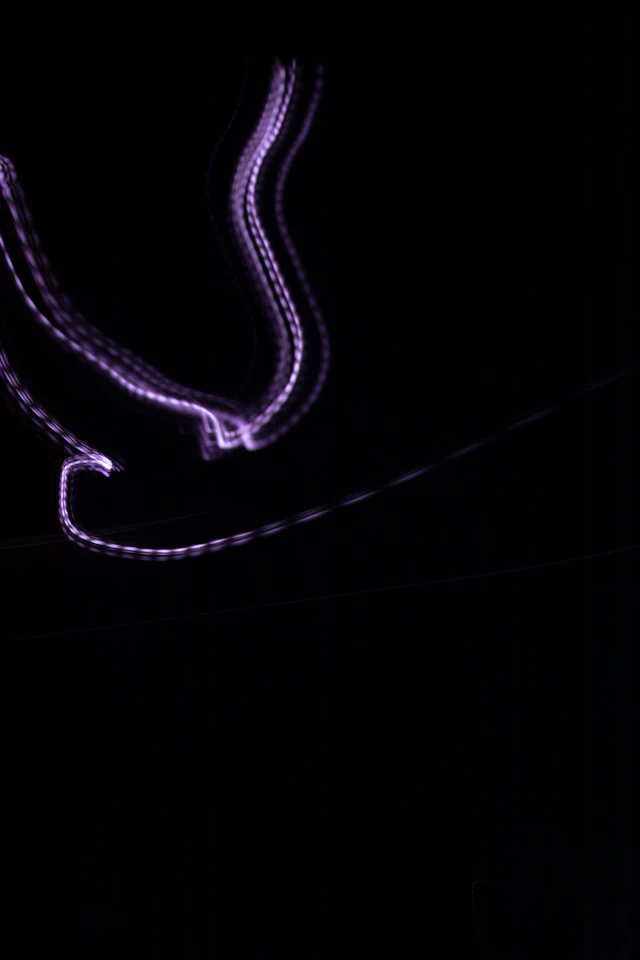 Traînées lumineuses violettes dessinant des courbes sur un fond noir.